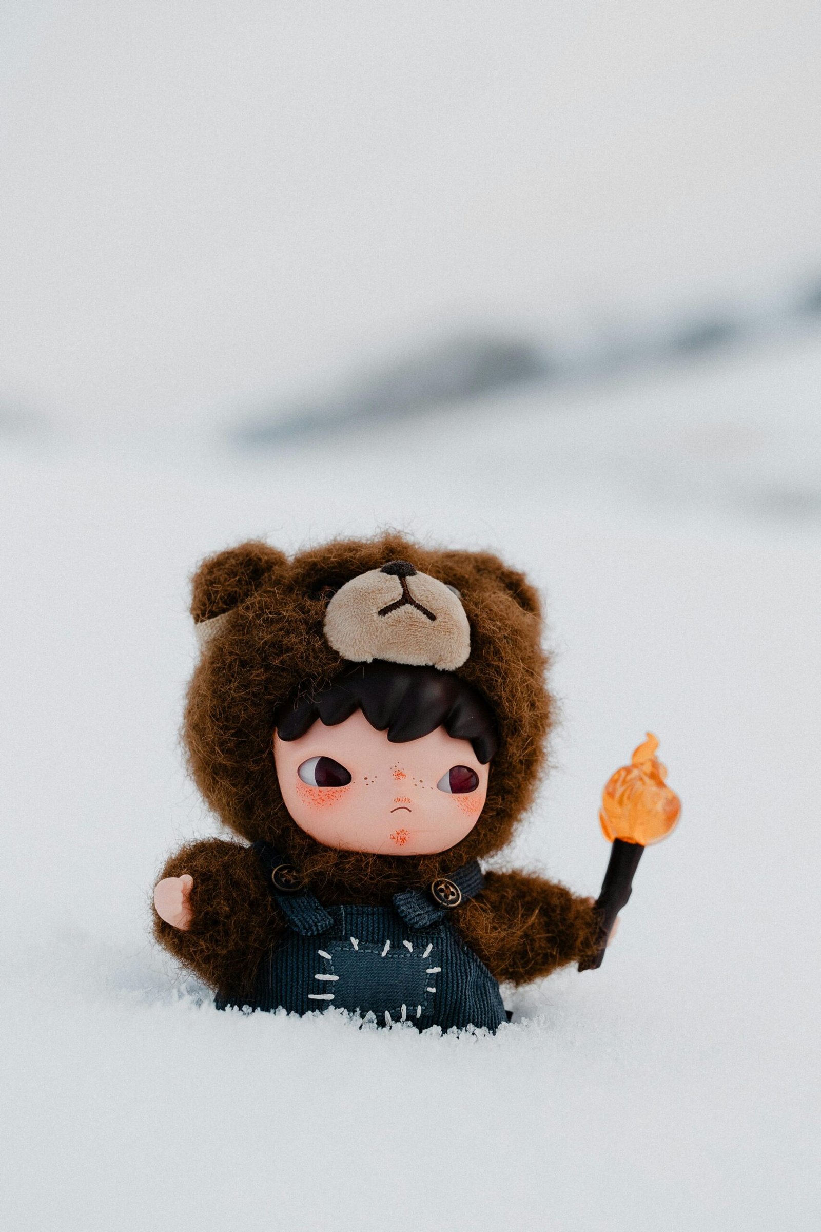 Cute childlike figurine in bear costume holding a torch on snow.